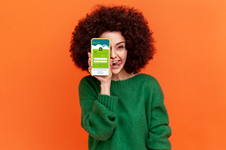Young women in green jersey holding a phone up to her face showing the Joy Pilot accounting software login page