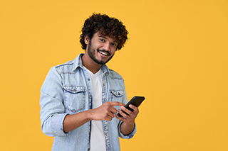 young guy in denim top smiling at you while using phone to input accounting information into joy pilot accounting software by using his phone