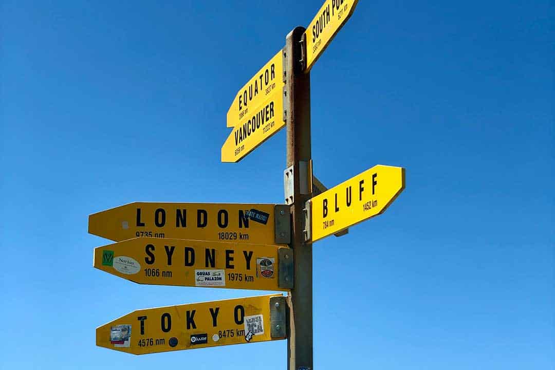 sign post with the names of different cities around the world and distance to them each on a sign pointing in the direction to that city